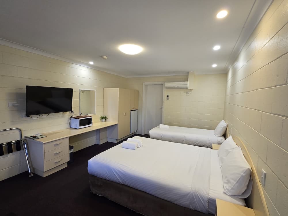 A clean, standard motel room with light cream, horizontal block-style walls and dark carpet.