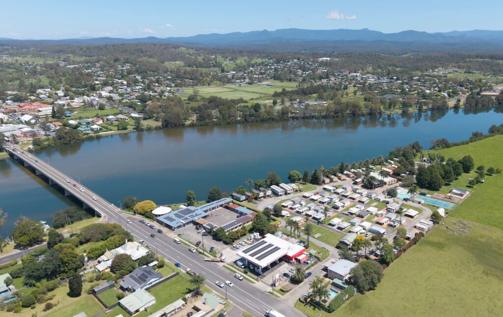A bright, sunny day shows a small town clustered along the banks of a wide, dark blue river.