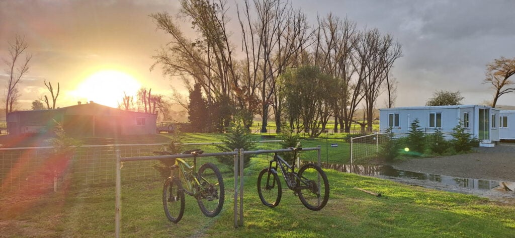 Two mountain bikes are hanging by their seats and front wheels on a low metal fence in a grassy area.